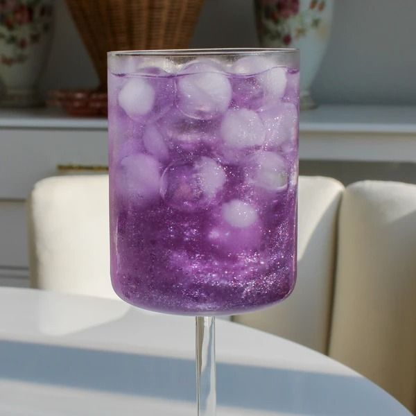 a glass filled with purple liquid sitting on top of a table next to a white chair