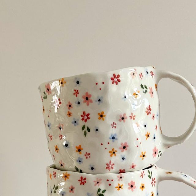 two coffee mugs are stacked on top of each other with colorful flowers painted on them