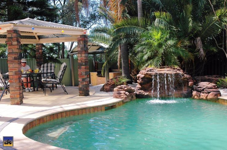 an outdoor pool with a waterfall and patio furniture in the back ground, surrounded by palm trees