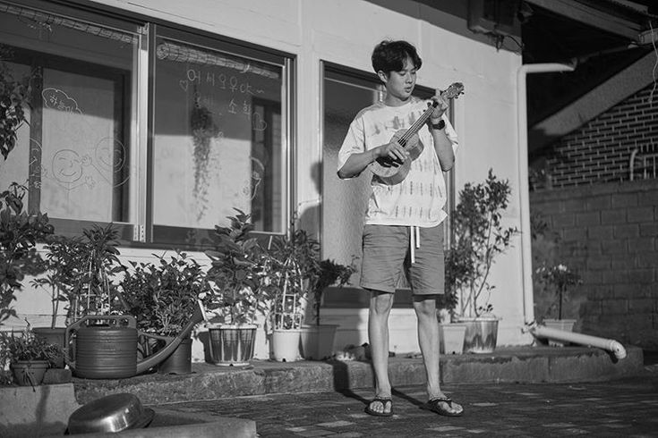 a young man is playing the guitar in front of a building with potted plants