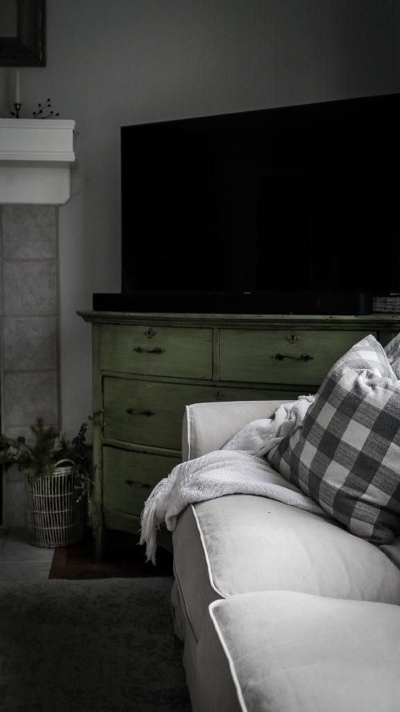 a living room with a white couch and green dresser in the corner, next to a flat screen tv