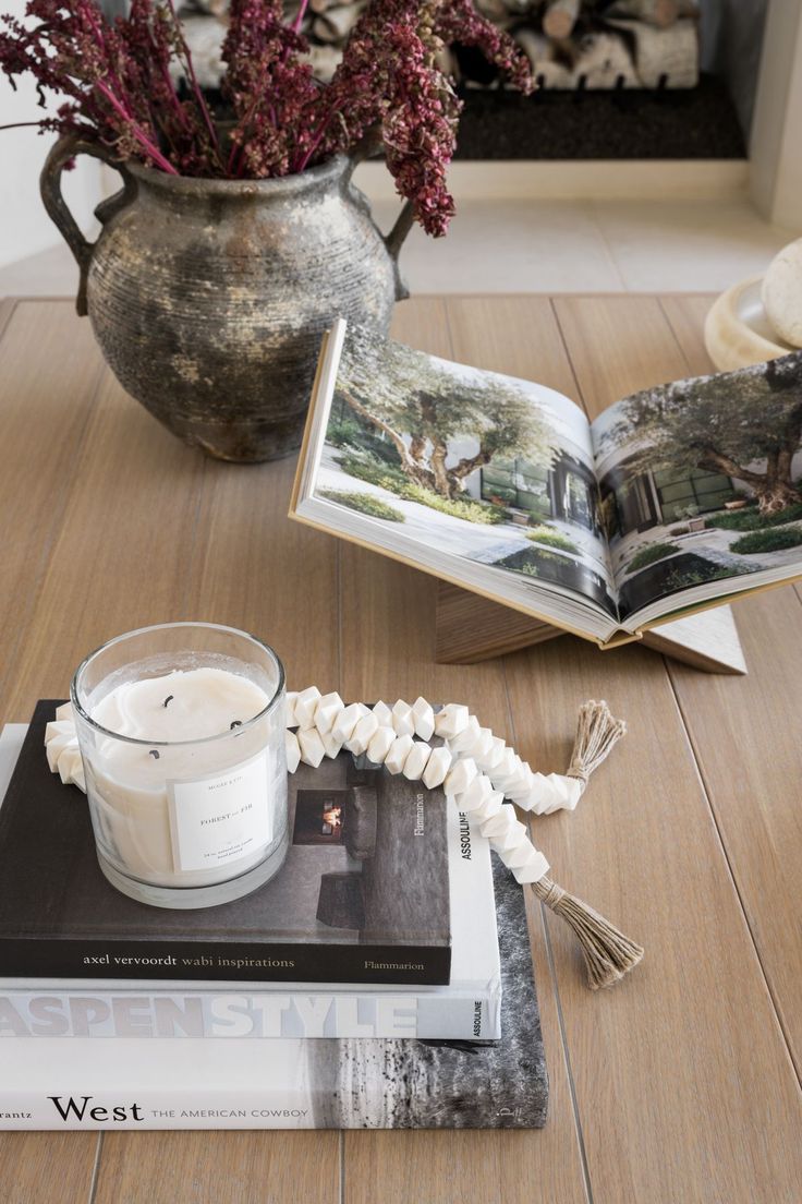 an open book on a table next to a candle and some flowers in a vase