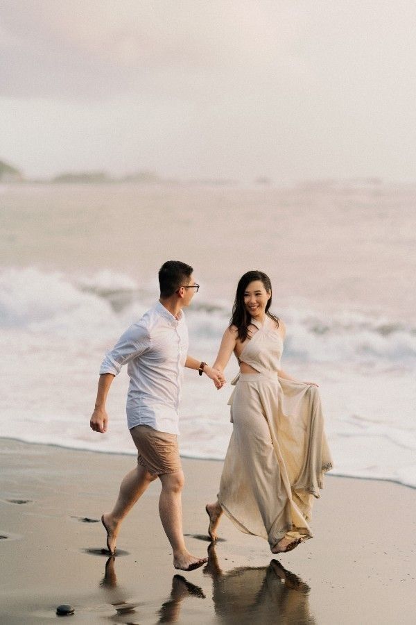 a man and woman walking on the beach holding hands