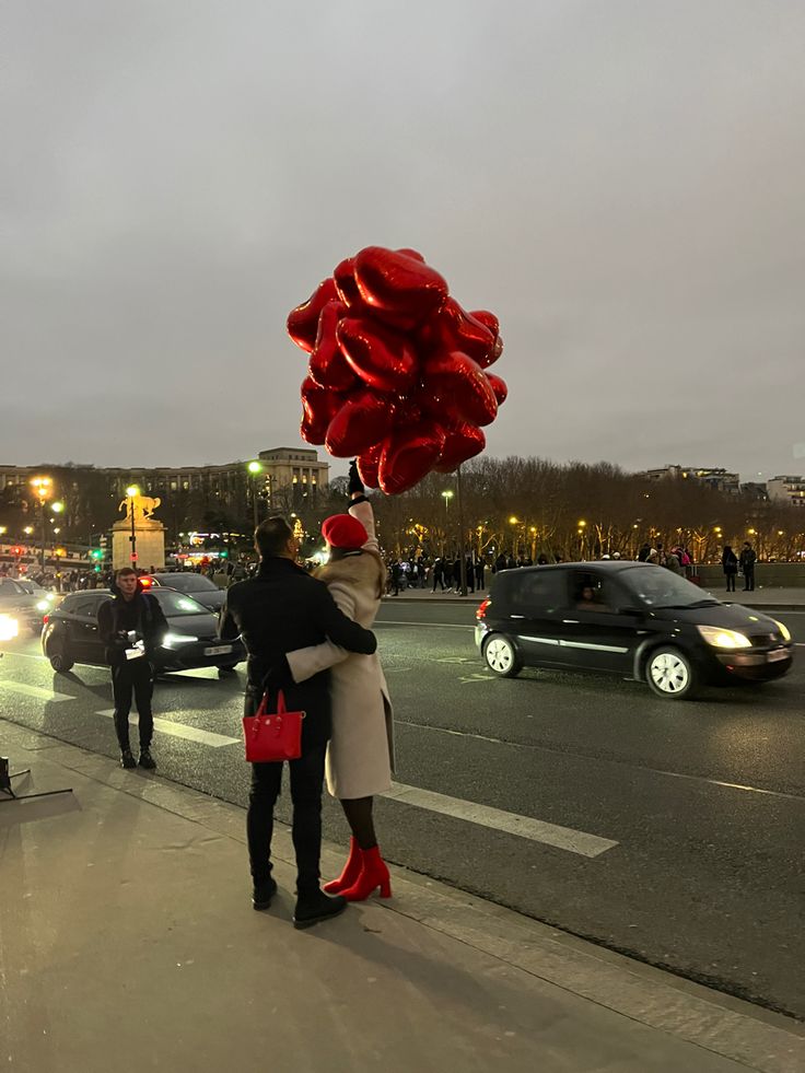 a man and woman standing on the side of a road with red balloons attached to their heads