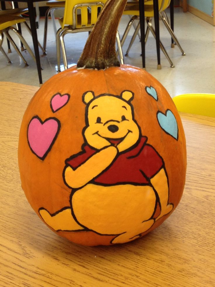 a winnie the pooh pumpkin sitting on top of a wooden table with hearts painted on it