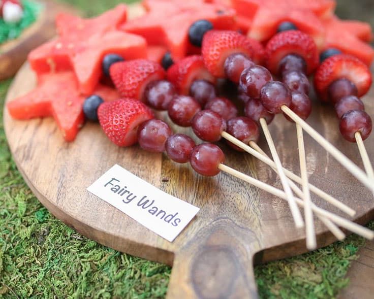 grapes, watermelon and strawberries are arranged on a cutting board with toothpicks