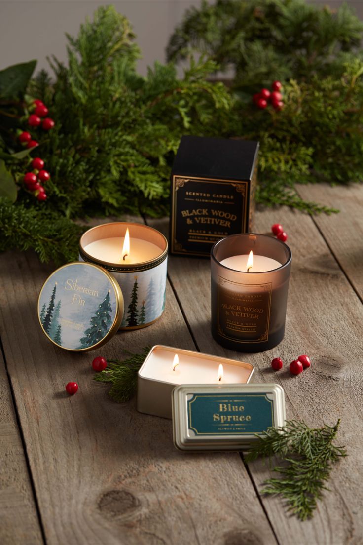 three candles sitting on top of a wooden table next to evergreen leaves and holly wreaths