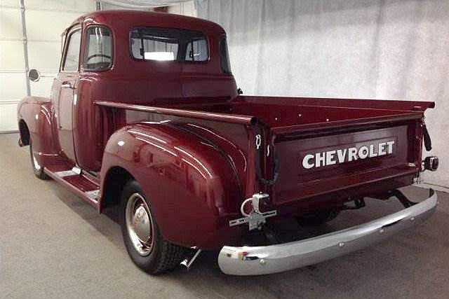 an old red chevrolet truck parked in a garage next to a white wall with the word chevy written on it