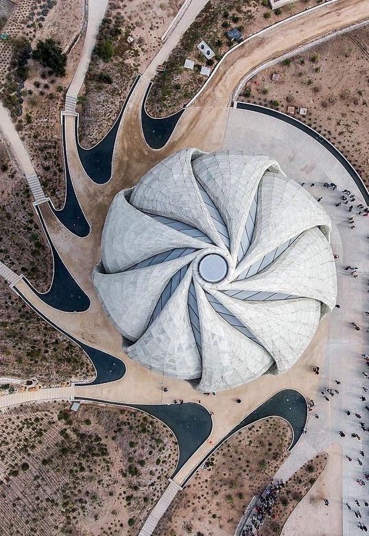 an aerial view of a circular structure in the middle of a desert with many people walking around it