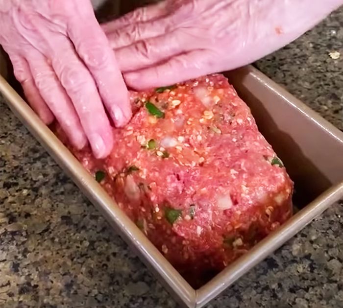 an older person reaching for a piece of meat in a box on a counter top