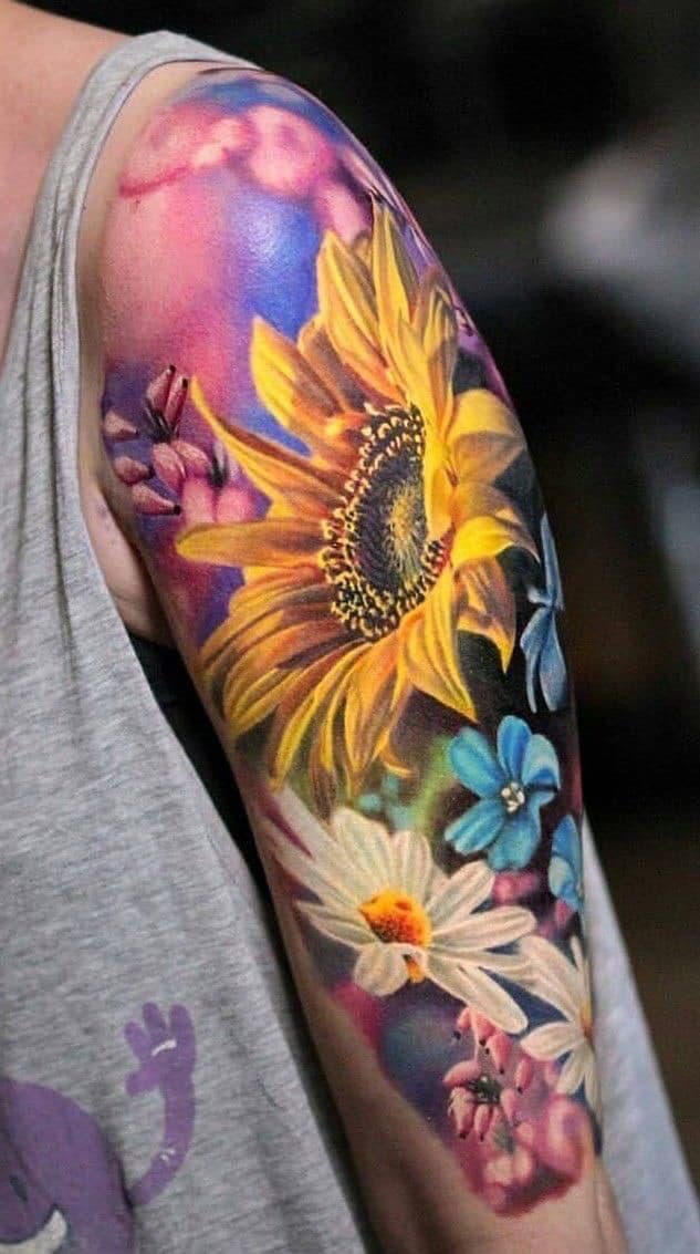 a man with a sunflower tattoo on his arm and shoulder is wearing a gray t - shirt