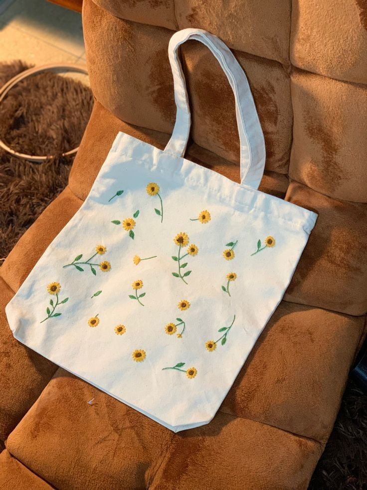 a white bag with sunflowers on it sitting on a brown chair in front of a window