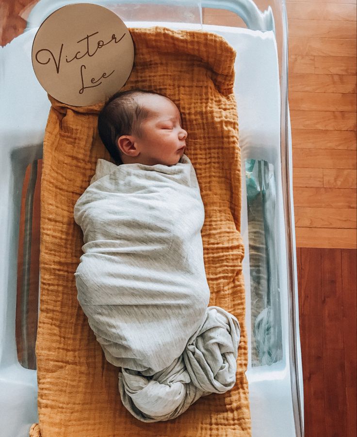 a baby wrapped in a blanket laying on top of a wooden floor next to a sign