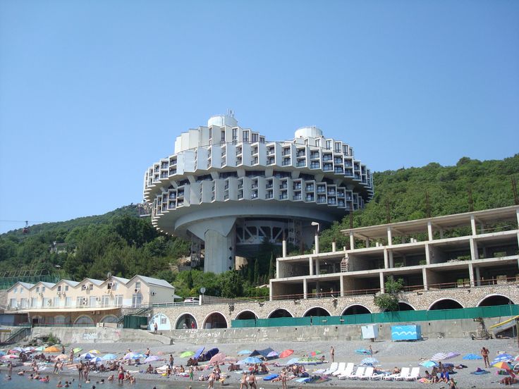 people are on the beach in front of a large building that looks like a circular structure