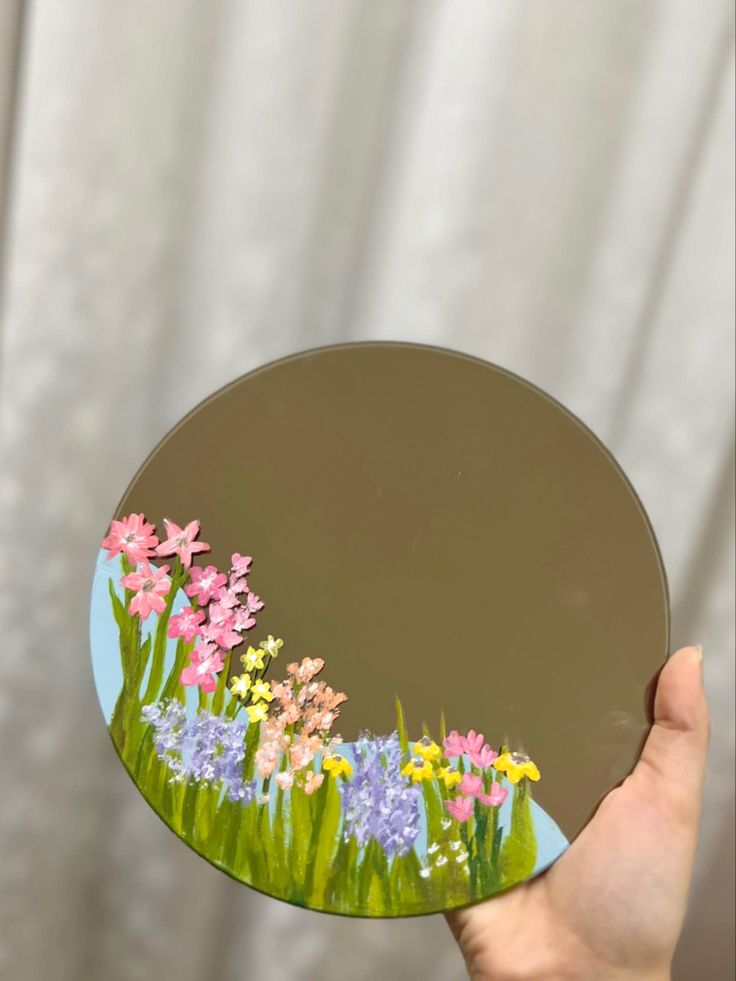 a hand holding a mirror with flowers painted on it