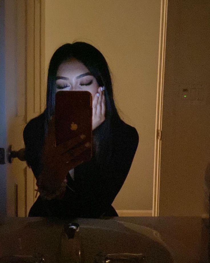 a woman looking at her cell phone while sitting in front of a sink with the light on