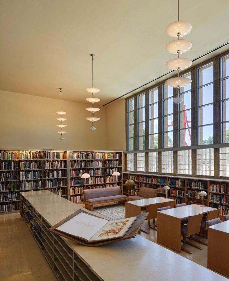 an empty library with tables, chairs and bookshelves in front of large windows