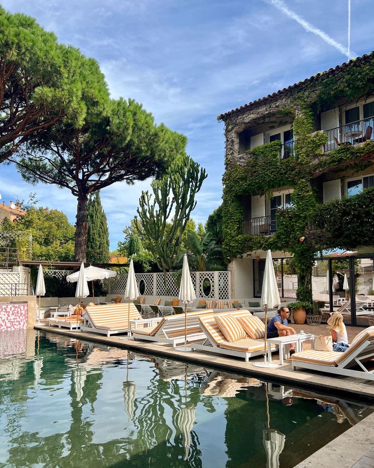 two people sitting on chaise lounges next to a pool in front of an apartment building