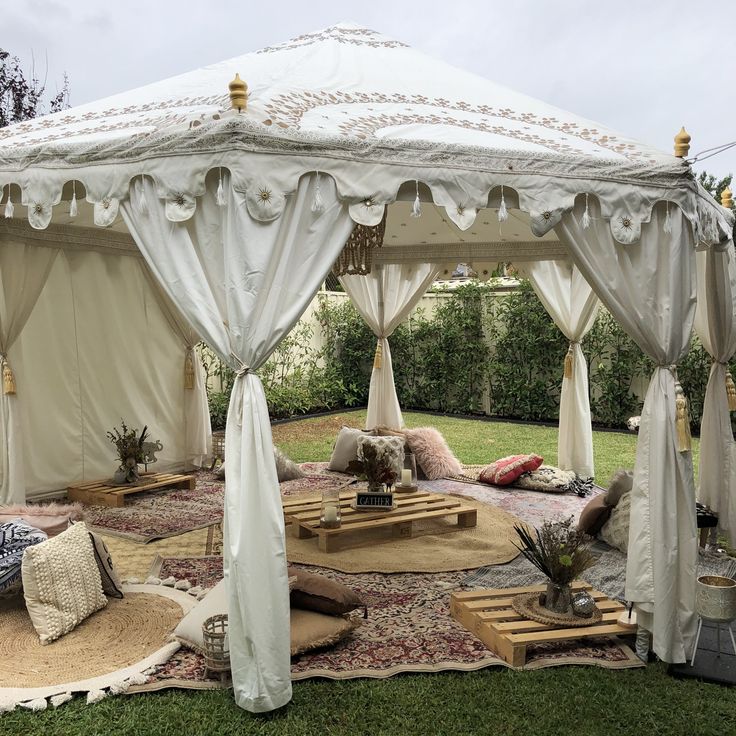 a white gazebo sitting in the middle of a lush green field with lots of pillows