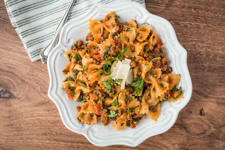 a white bowl filled with pasta and meat on top of a wooden table next to a fork