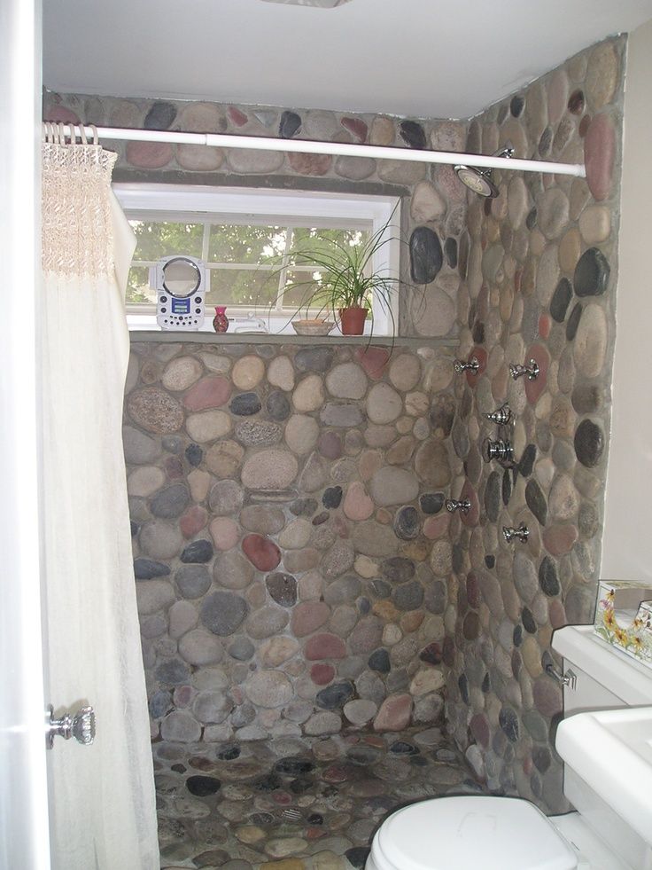 a bathroom with stone walls and flooring next to a white toilet sitting under a window