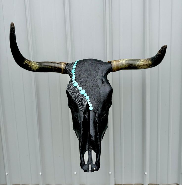 a cow skull with turquoise beads on it's antlers is shown in front of a white wall