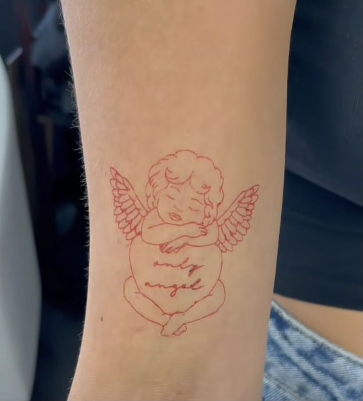 a small tattoo on the arm of a woman with an angel sitting on her knees