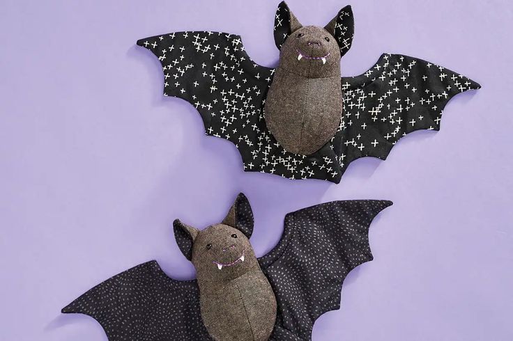 two stuffed bats sitting next to each other on top of a purple surface with black and white designs