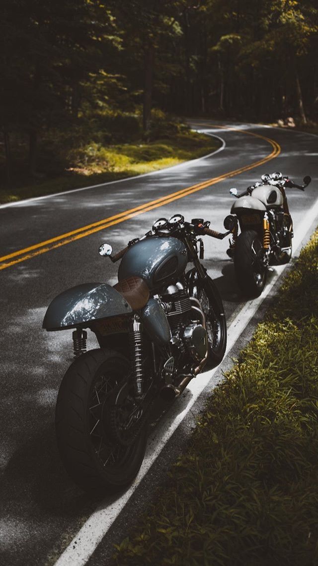 two motorcycles are parked on the side of the road in front of some grass and trees