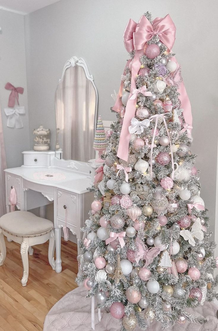 a white christmas tree with pink and silver ornaments in a girls'bedroom, next to a dressing table