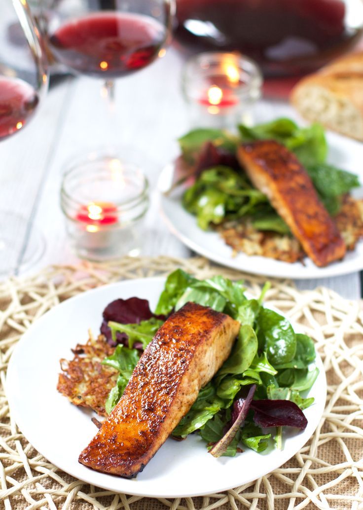 two white plates topped with fish next to salad and wine glasses on a wicker table cloth