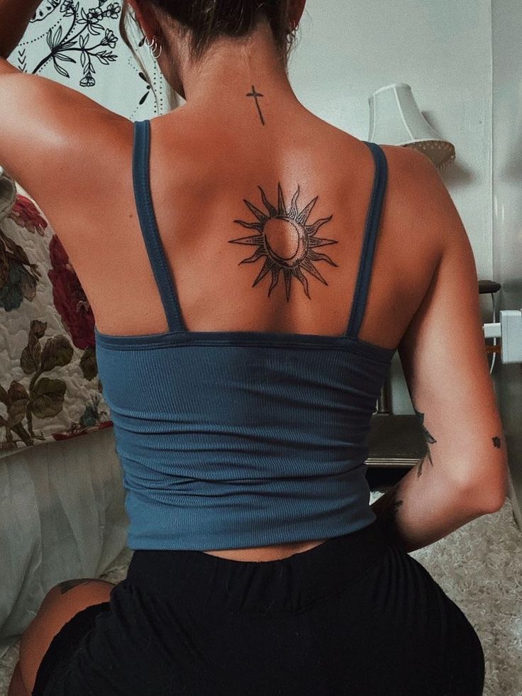 a woman with a cross tattoo on her back sitting in front of a couch and looking at the camera