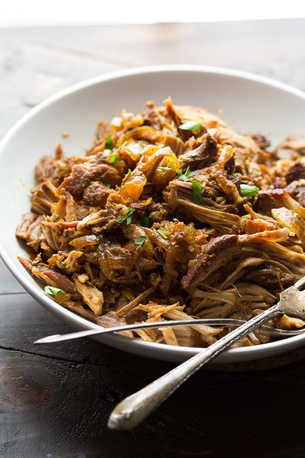 a white bowl filled with meat and vegetables on top of a wooden table next to two spoons