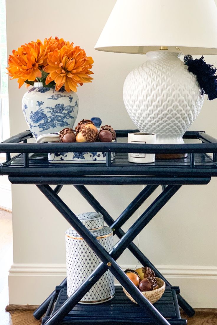 a blue and white table with orange flowers in vases on it, next to a lamp