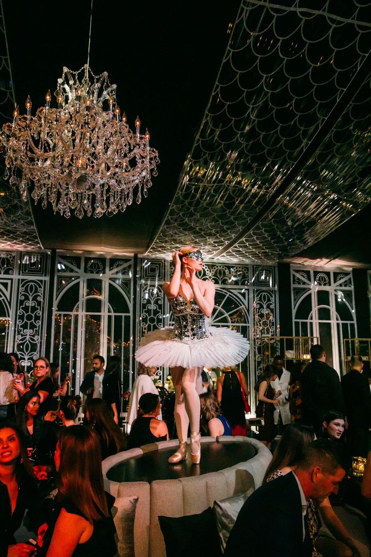 a ballerina is standing on top of a table in a room full of people