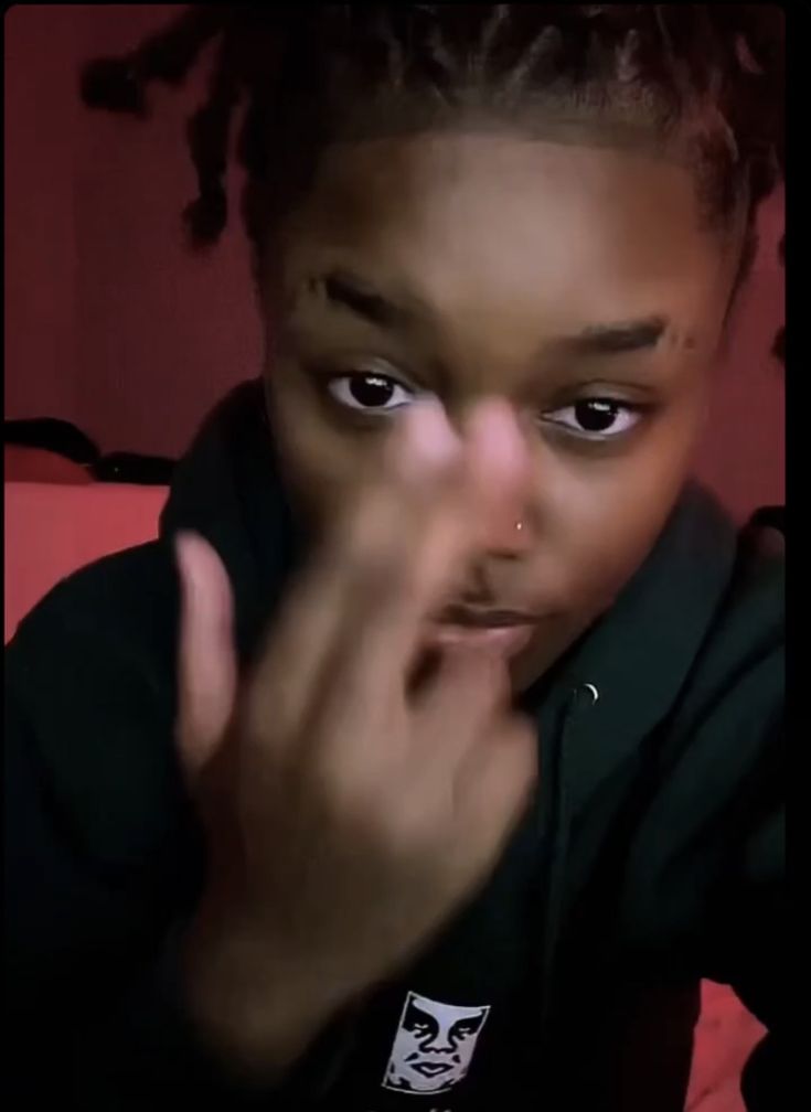 a young woman with dreadlocks making a hand gesture to the camera while wearing a black shirt