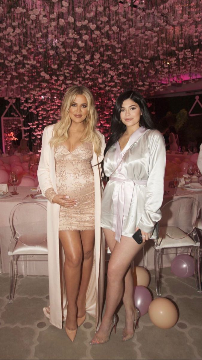 two beautiful women standing next to each other in front of balloons and chandeliers