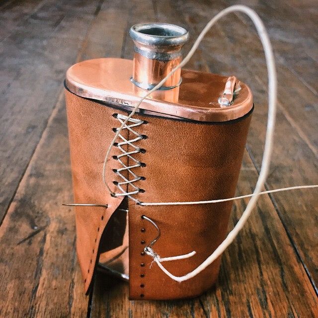 a brown leather flask with a rope wrapped around it on a wooden table top