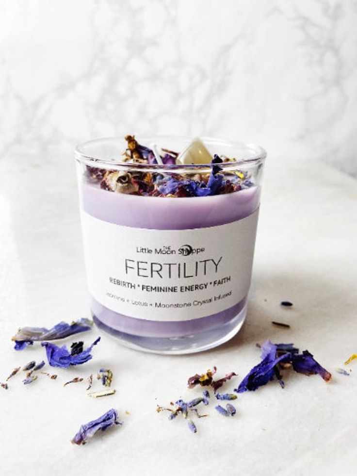 a glass jar filled with purple flowers on top of a white counter next to dried petals