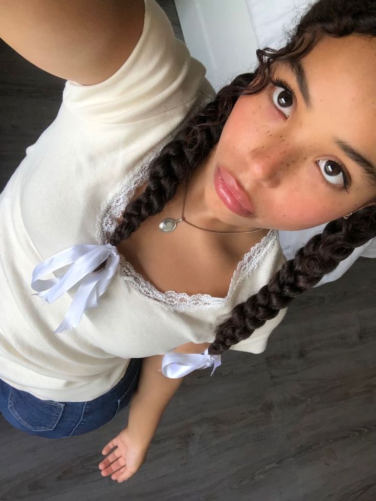 a girl with braids and a white shirt is looking up at the camera while standing in front of a mirror