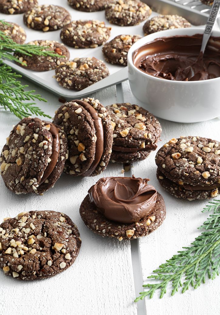 cookies with chocolate frosting and sprinkles on a white wooden table next to evergreen branches