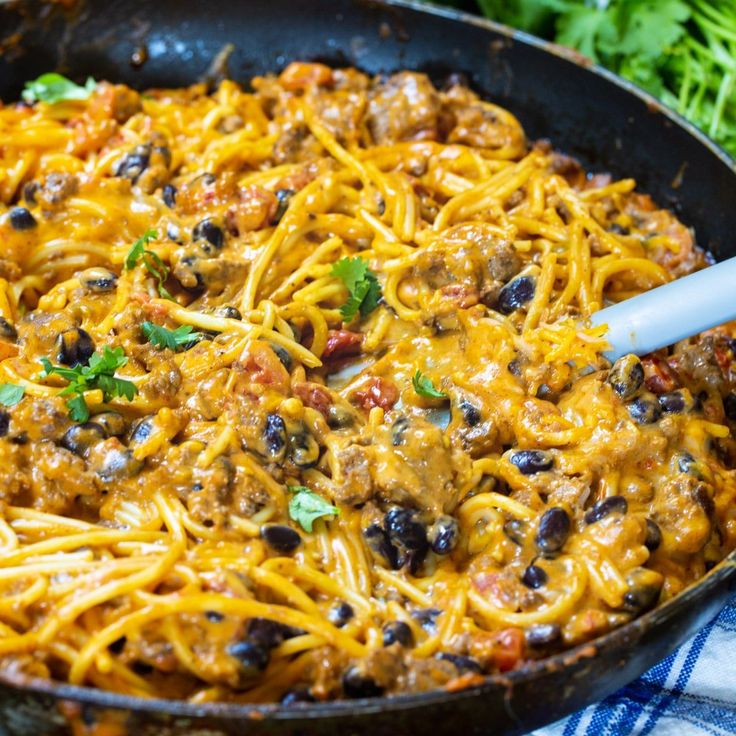 a skillet filled with spaghetti and meat covered in cheese, black olives and cilantro