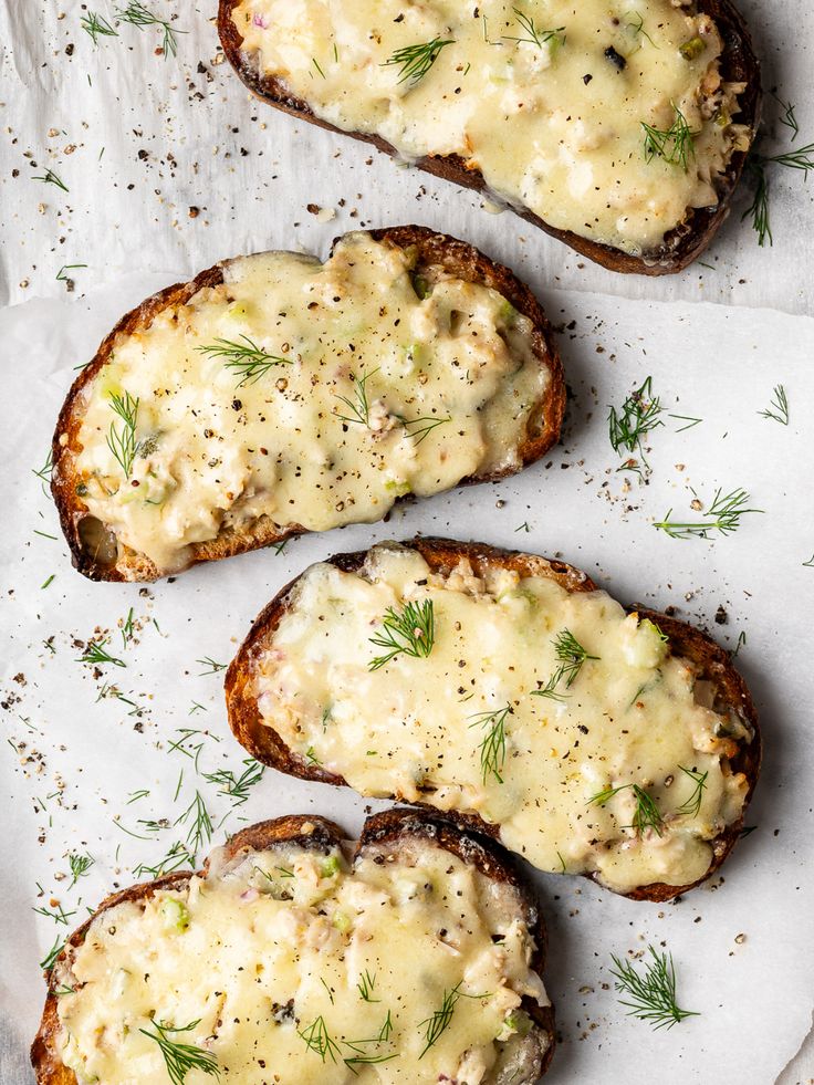 four pieces of bread with cheese and herbs on them sitting on a piece of parchment paper