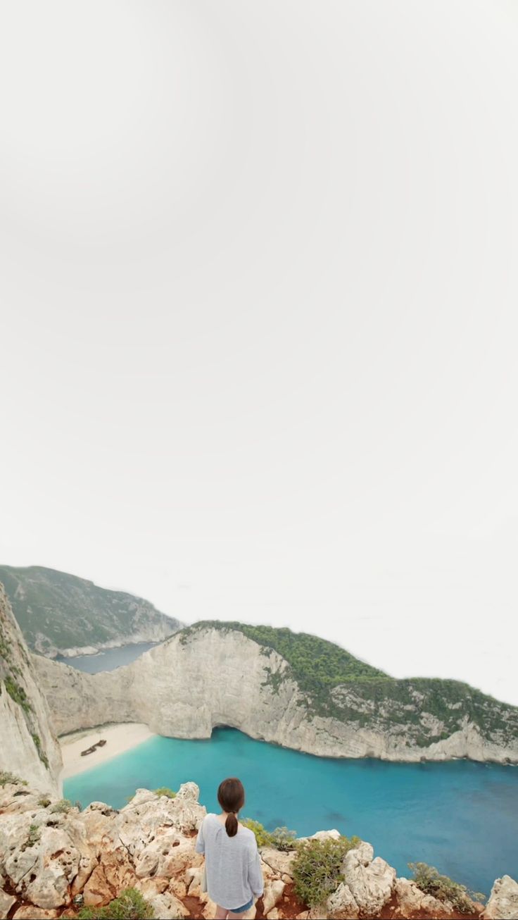 a man sitting on the edge of a cliff looking at a body of water