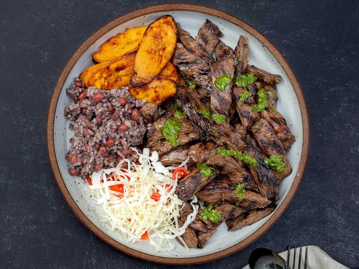 a white plate topped with meat, beans and veggies next to sliced bananas