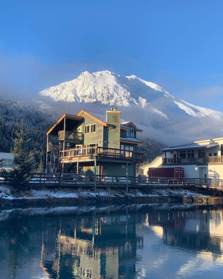 a large house sitting on top of a lake next to a snow covered mountain in the background