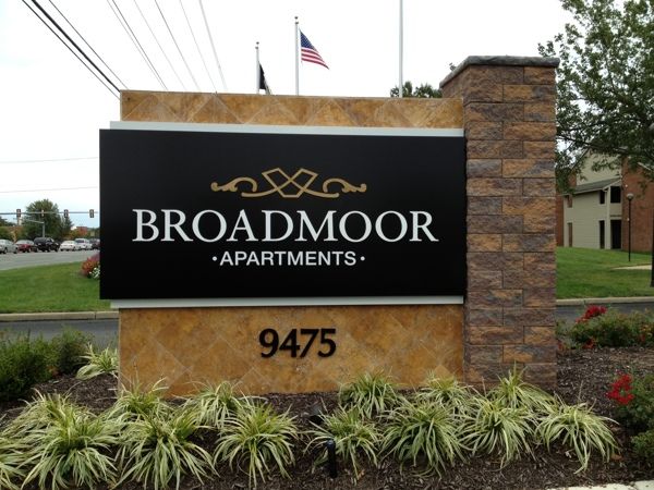 the sign for broadmore apartments in front of an american flag and some flowers outside