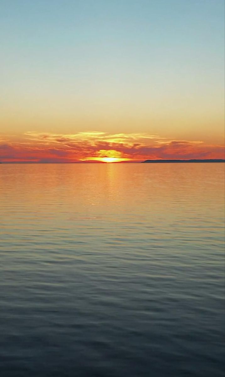 the sun is setting over the ocean with calm water