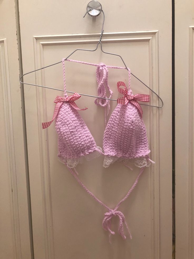 two pink crocheted baby hats hanging from a hook on a door hanger