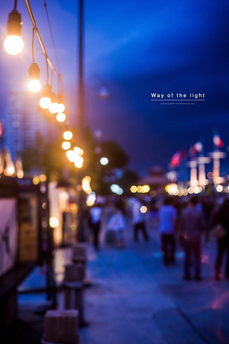 many people are walking down the street at night time, with lights hanging above them